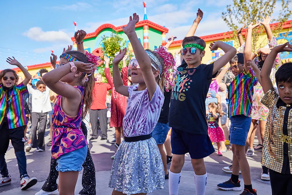 Kinder tanzen mit Sonnenbrillen und Festival-Kostümen auf dem LEGO Festival